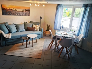 Ferienwohnung in Saal mit Blick ins Wohnzimmer wo man eine blaue Couch und einen Tisch mit Stühlen am Fenster sehen kann.